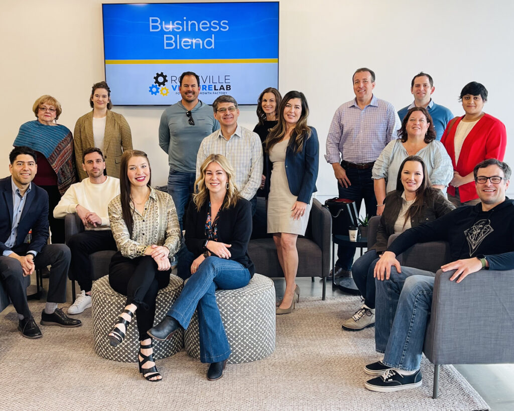 Photo of Krista and Kayla sitting amongst a group of people in front of a monitor that reads "Business Blend"